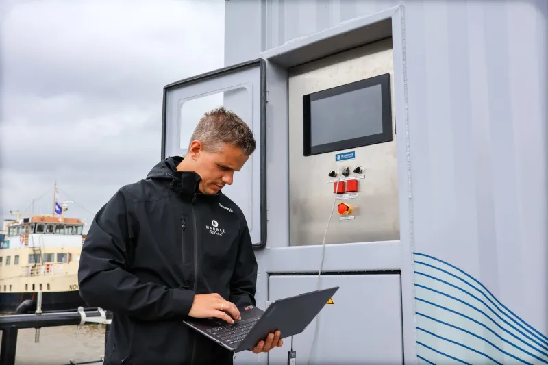 Engineer van Marble werkt op een laptop naast een rvs-bedieningspaneel op de kade