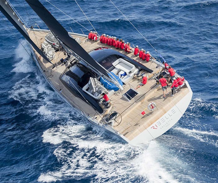 Zeiljacht Ribelle helt over op zee met bemanning in het rood langs de reling