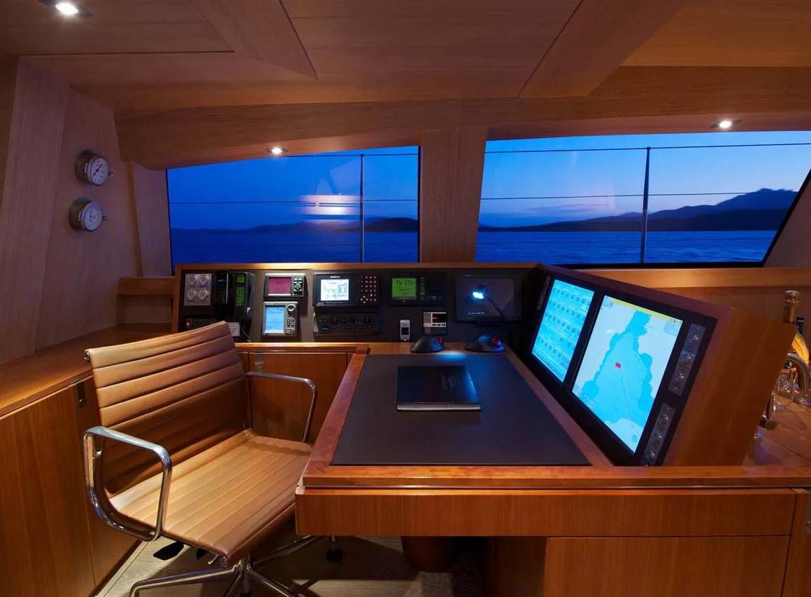 Stuurhuis van een jacht bij schemering met houten brugconsole, navigatieschermen en stuurstoel