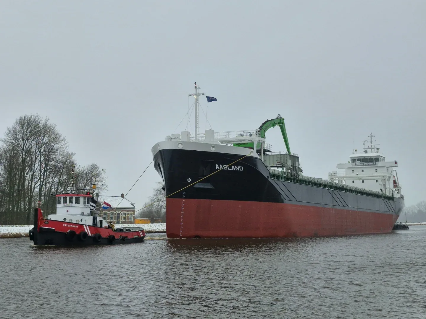 Cargo vessel Aasland towed through a snowy canal by a tug on the way to sea trials
