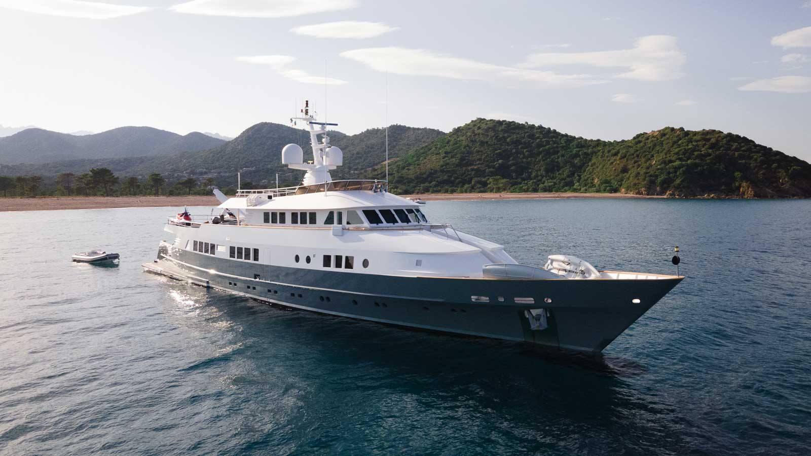 45-metre motor yacht Berzinc at anchor in a calm bay with green hills