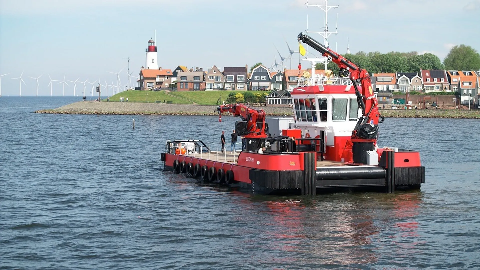 Red multicat Leon H. with deck cranes sailing past the lighthouse of Urk