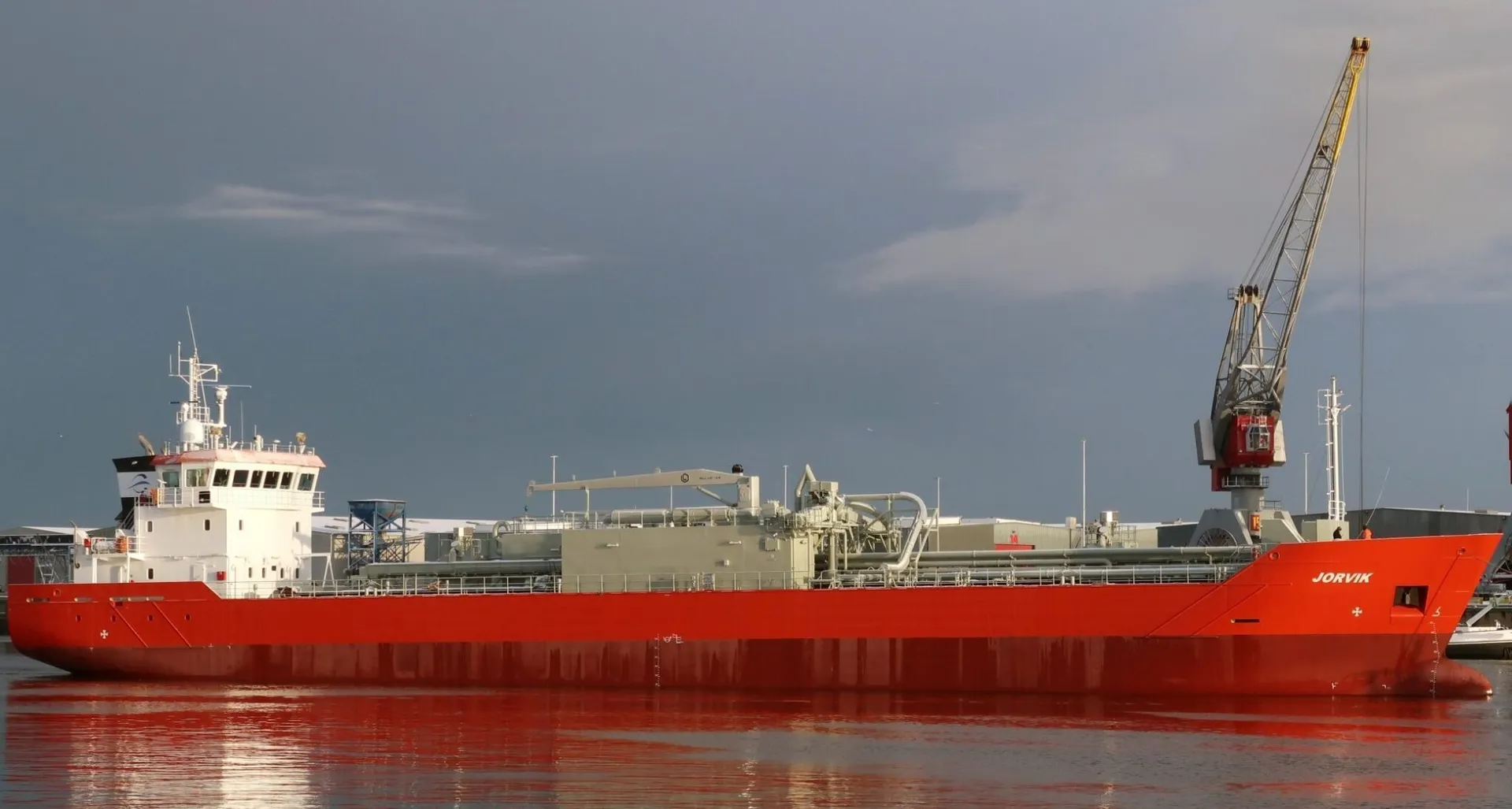 Red cement carrier Jorvik moored in port beside a harbour crane